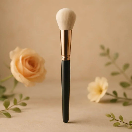 Pinceau maquillage à manche noir et doré, fleurs roses en fond, ambiance élégante.