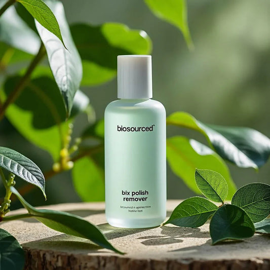 Flacon de dissolvant à ongles biosourced posé sur une souche, entouré de feuilles vertes.